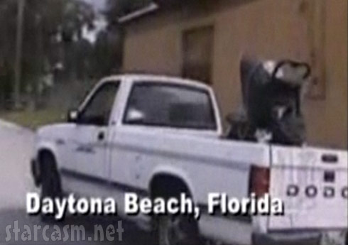 A baby riding in the back of a pick up truck in a baby stroller